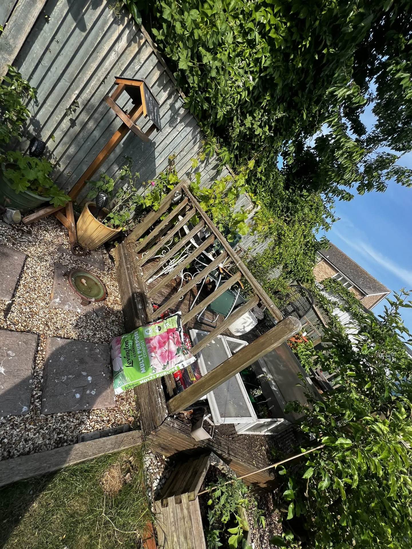 The worn original deck stacked with plant pots, a cold frame and garden tools before construction began