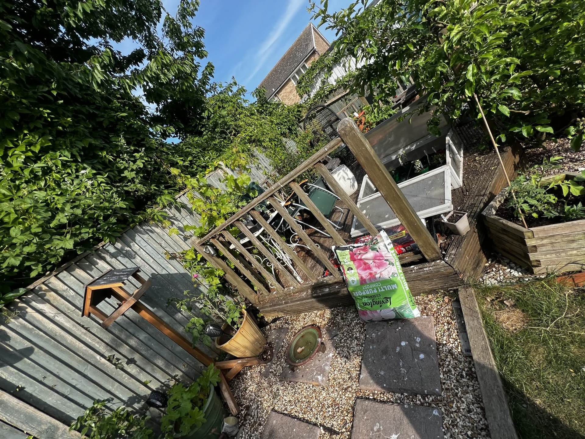 The cluttered old deck and side patio area, with a compost bag and cold frame, before the rebuild