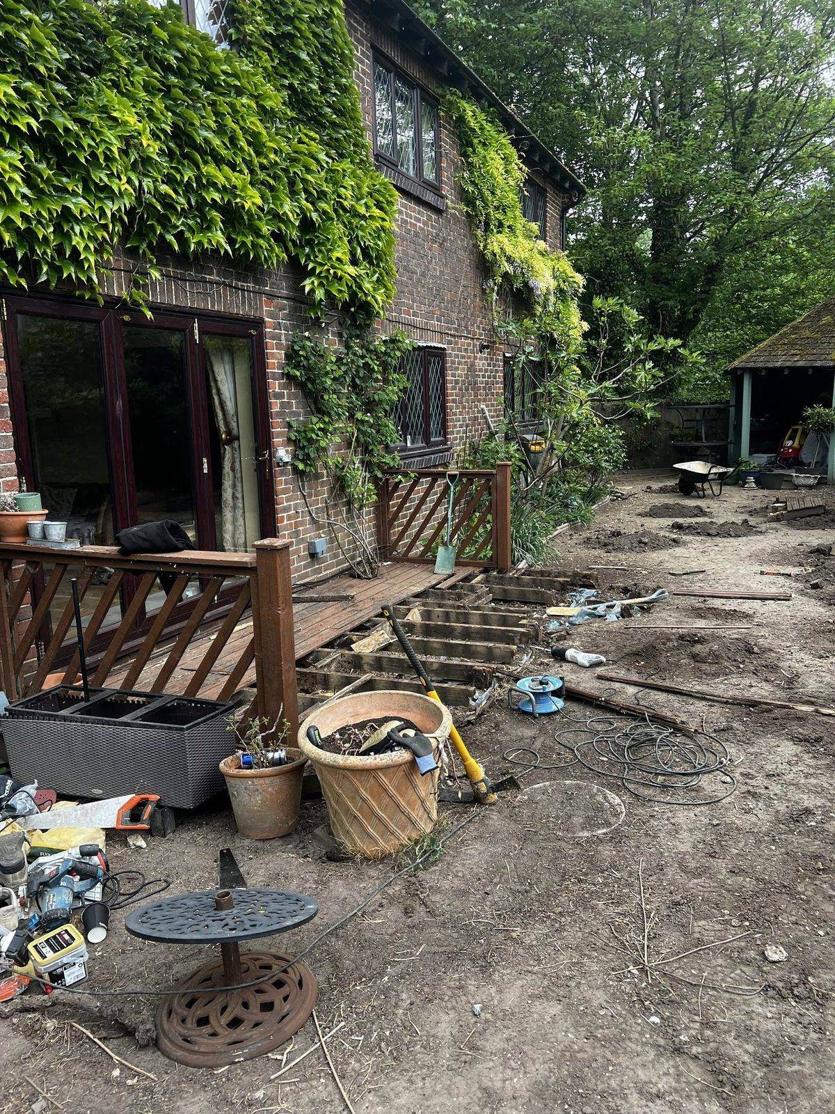 The old deck partially stripped back to its joists, with the cleared groundwork area and established brick property behind